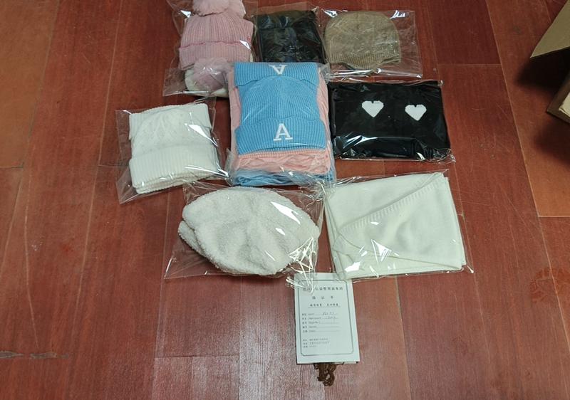 Multiple packaged knit beanies and scarves in pink, blue, black, cream, and tan colors displayed on wooden floor with product card - wholesale price for Middle East buyers