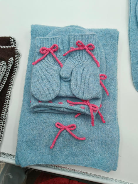 Baby blue knitted winter gift set including scarf, beanie hat and mittens with pink bow embellishments, displayed flat - wholesale price for Europe buyers