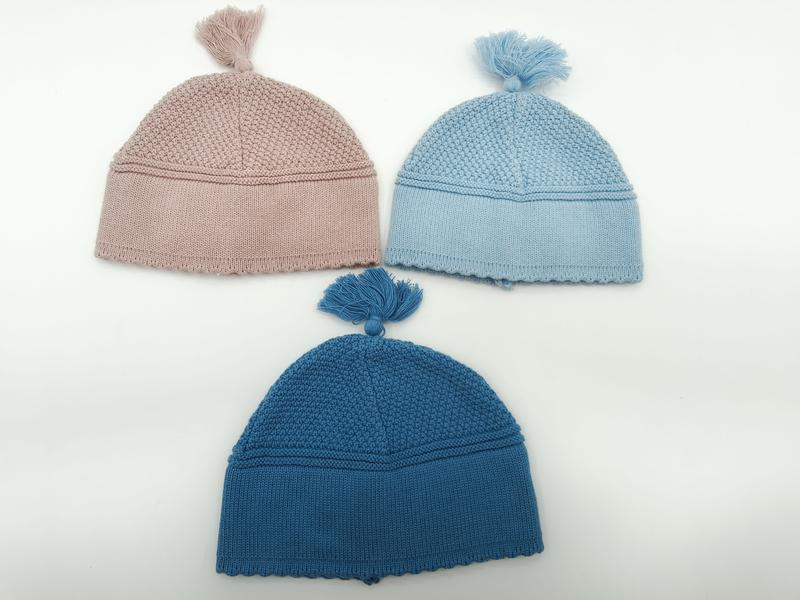 Three knitted baby beanies with tassels in dusty pink, light blue, and teal blue arranged on white background - custom packaging design free
