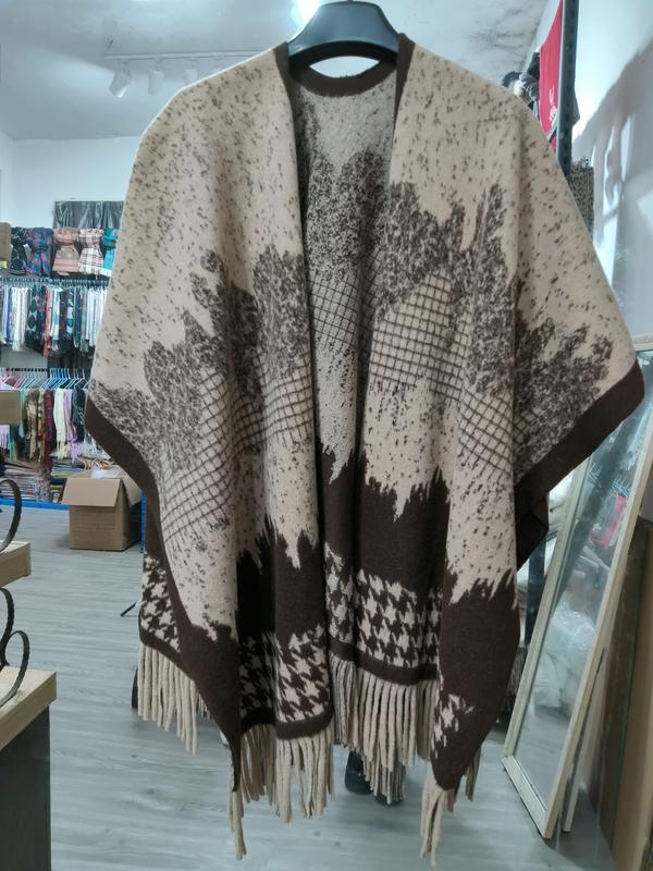 Beige and brown jacquard knit open-front poncho cape with floral pattern, houndstooth border, and fringe hem on hanger - email us get price list now