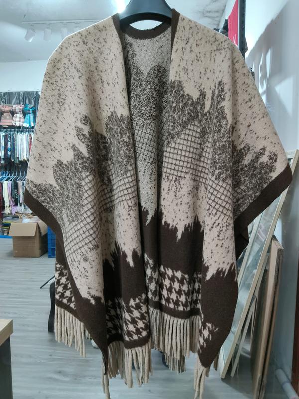 Oversized knit poncho cape in beige and brown with leaf print, houndstooth border, and fringe hem on hanger - request quote reply same day