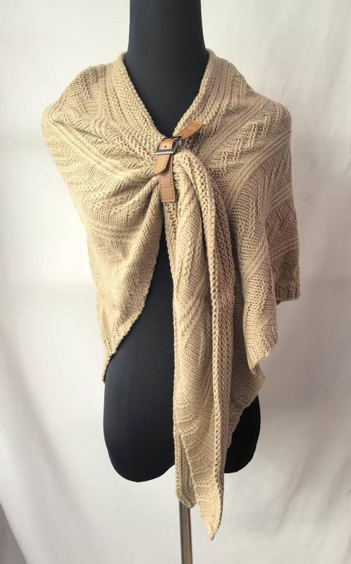 Beige cable knit wrap shawl secured with tan leather buckle clasp displayed on black mannequin torso - retail buyer inquiry welcome - request quote reply same day