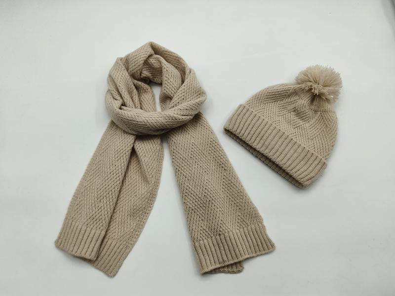 Beige chunky knit scarf coiled and matching pom-pom beanie hat set on white background - event merchandise supplier