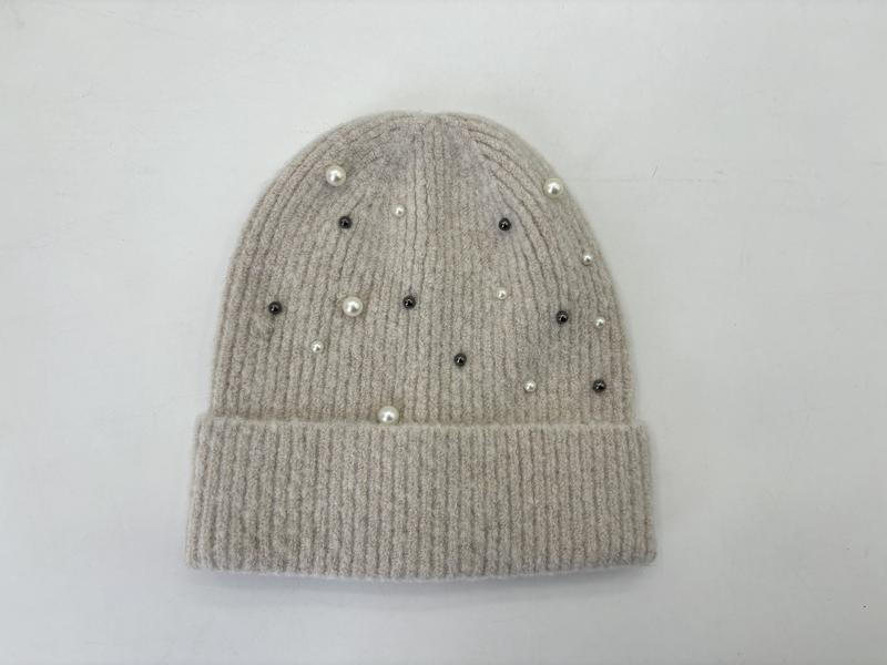 Flat lay of a beige ribbed knit beanie hat decorated with scattered white pearls and dark crystal studs on white background - corporate gift customization