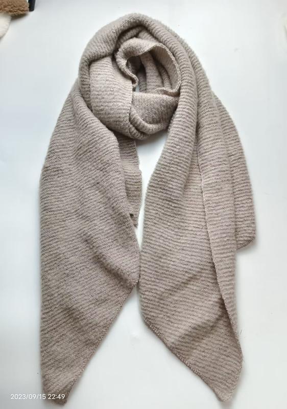 Beige ribbed knit scarf loosely wrapped and laid flat on white surface, showing soft textured stripe pattern - event merchandise supplier