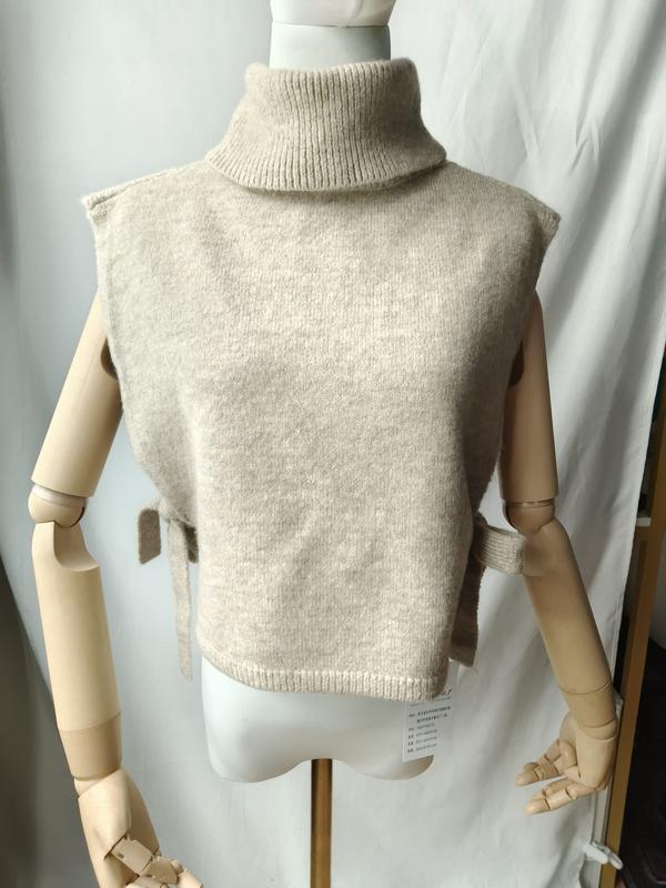 Beige knit sleeveless turtleneck sweater vest with side tie details displayed on a mannequin, soft wool blend - ISO 9001 quality controlled
