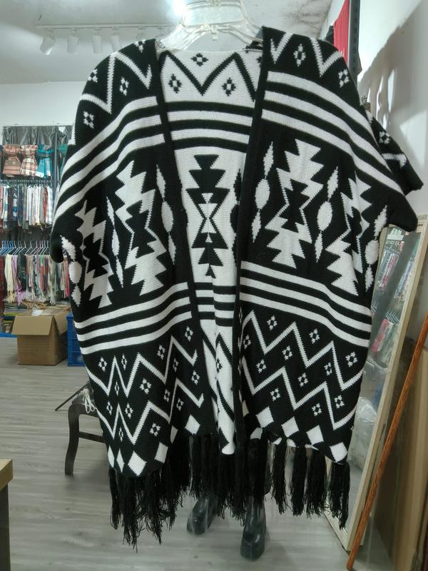 Black and white Aztec geometric pattern knit poncho cape with tassel fringe hem displayed on hanger in store - boutique retail bulk order