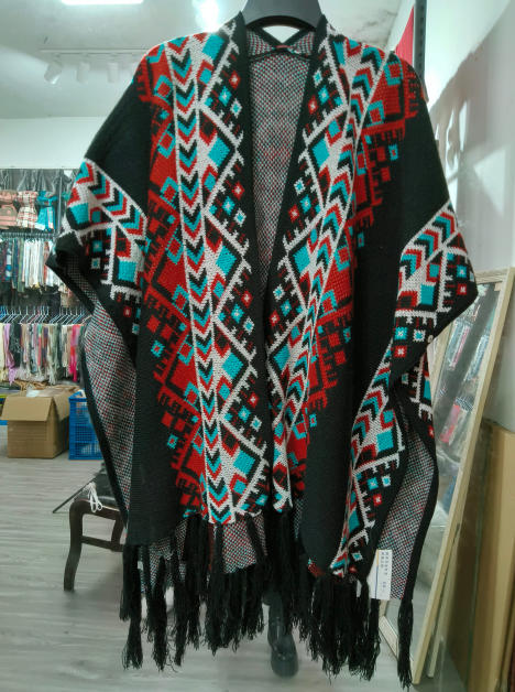 Black open-front knit poncho with red teal white Aztec geometric pattern and fringe hem displayed on hanger - ODM OEM service available - corporate gift customization