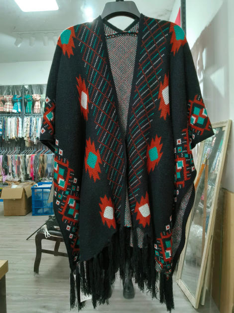 Black knit open-front poncho cape with teal, rust and white Aztec geometric pattern and fringe hem on hanger - event merchandise supplier
