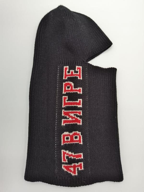 Black ribbed knit balaclava ski mask laid flat showing red and white varsity-style letter graphics on dark wool fabric - certified scarf manufacturer China - gift shop wholesale supplier