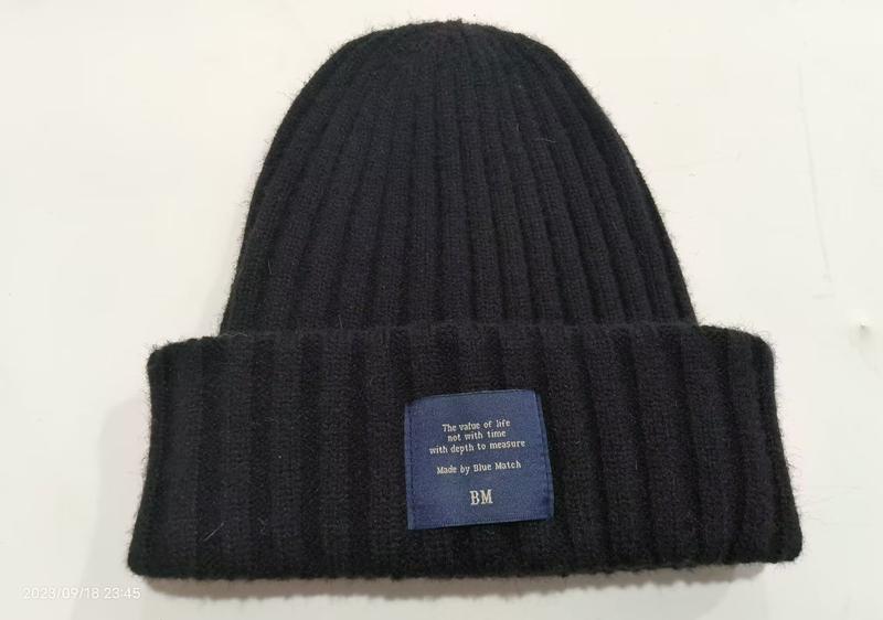 Black chunky ribbed knit winter beanie hat with folded cuff and blue brand label on white background - sample order 10pcs available