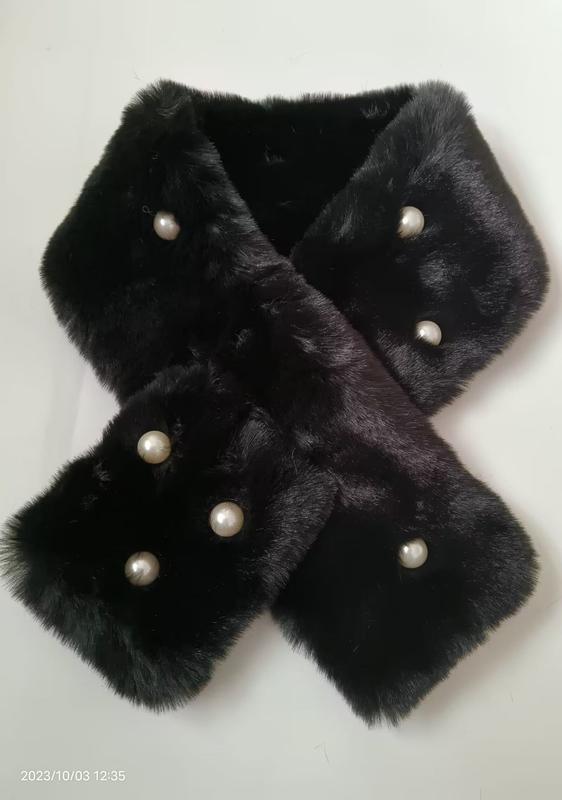 Black faux fur crossover neck scarf with decorative white pearl buttons laid flat on white background - hotel amenity scarf supplier