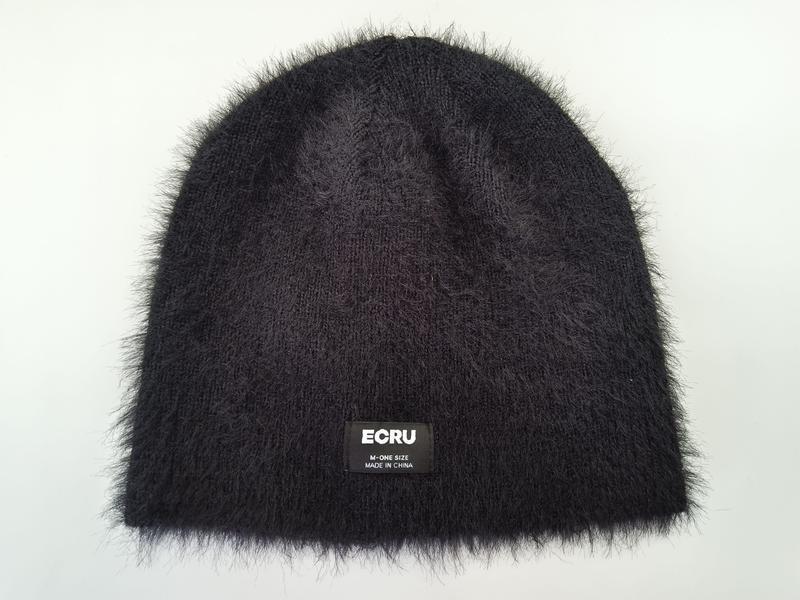 Black fluffy knit beanie hat with furry texture and small label patch, laid flat on white background - boutique retail bulk order