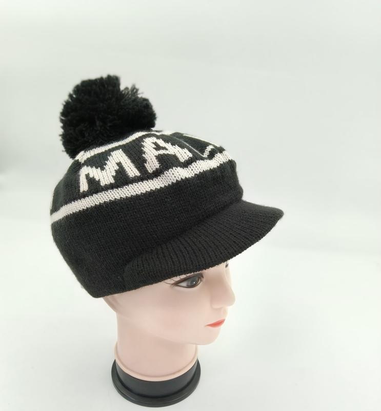 Black knitted pom-pom beanie with brim visor and bold white letter jacquard pattern displayed on mannequin head - free sample within 7 days