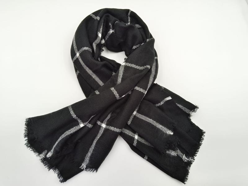 Black woven scarf with white and gray plaid grid pattern, tied in a loose knot, with fringe edges on white background - EU REACH compliant material
