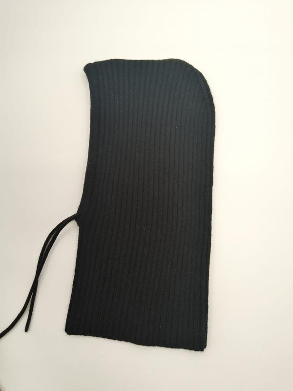 Black ribbed knit balaclava ski mask laid flat on white surface showing curved hood opening and drawstring tie detail - private label service available