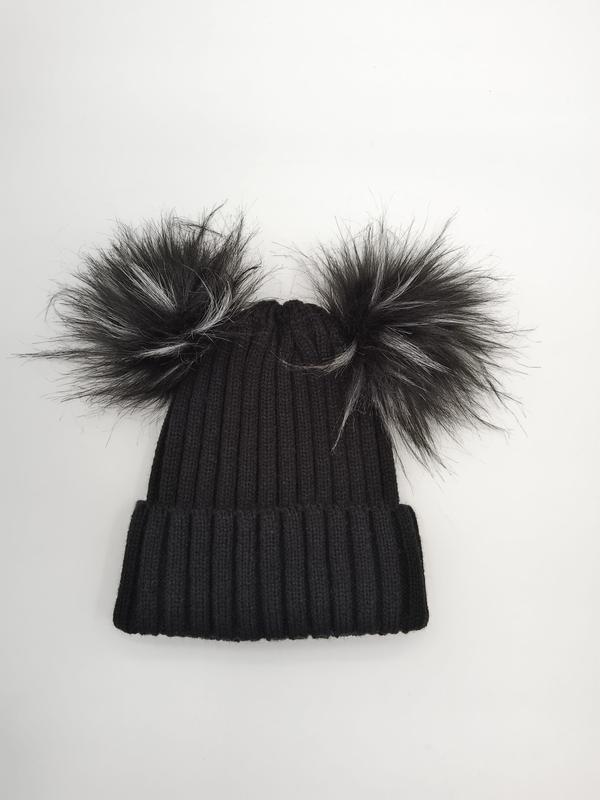 Black ribbed knit winter beanie hat with two large faux fur pom poms on top, laid flat on white background - free sample within 7 days