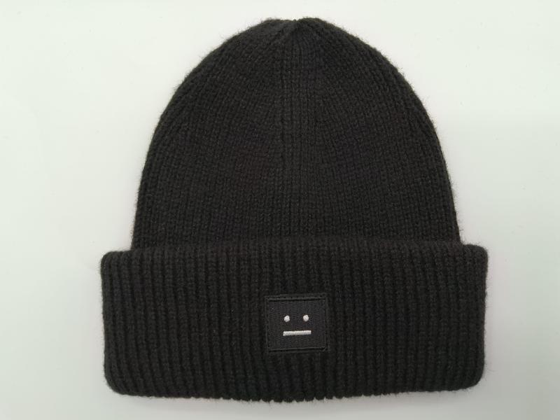 Black ribbed knit beanie hat with folded cuff and small embroidered face patch logo on white background - small batch 100pcs accepted
