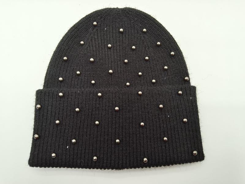 Black ribbed knit beanie hat covered with scattered silver metal studs and a folded cuff, laid flat on white background - gift shop wholesale supplier