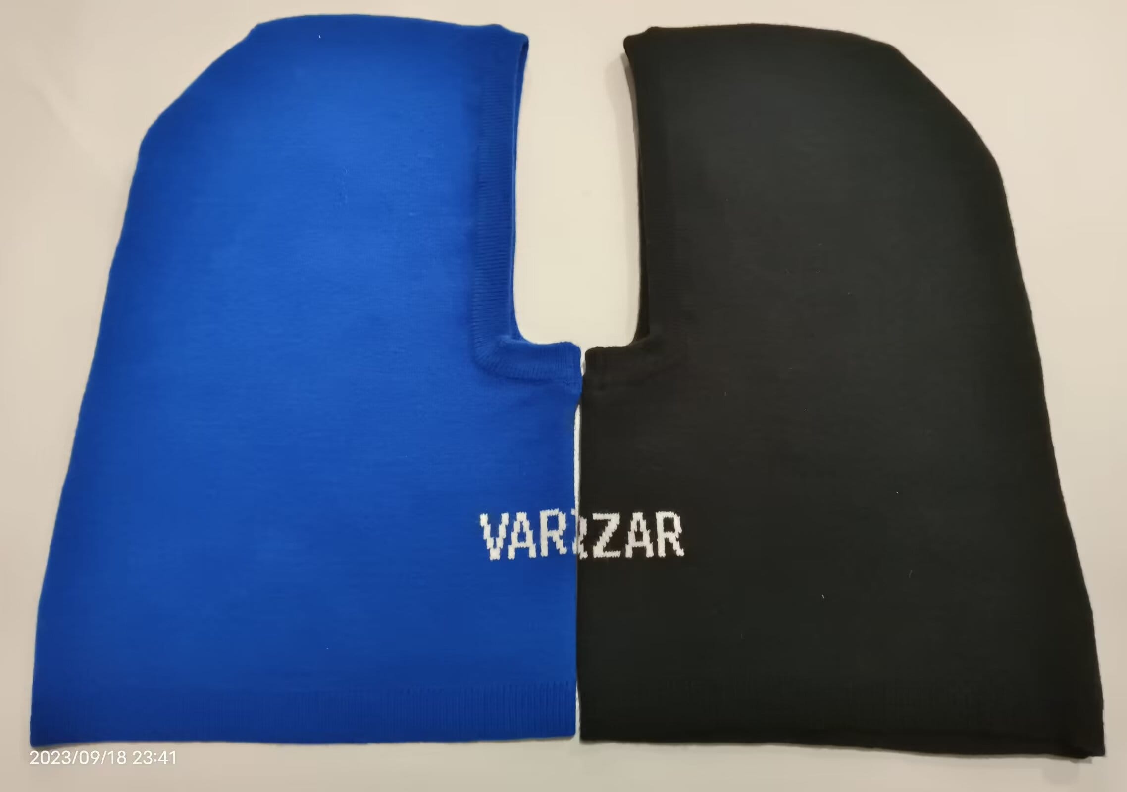 Blue and black two-tone knit balaclava laid flat showing face opening and brand logo on black side - MOQ 100pcs mixed colors OK