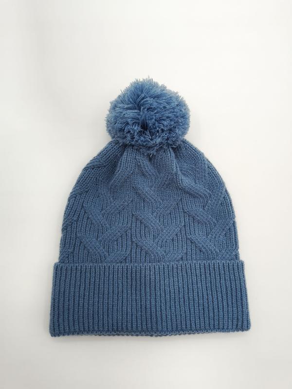 Steel blue cable knit winter beanie hat with fluffy pom pom on top and ribbed cuff, laid flat on white background - request quote reply same day