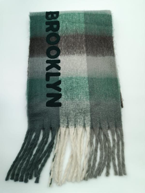 Folded green grey and cream plaid scarf with Brooklyn embroidered lettering and fringe tassels on white background - event merchandise supplier