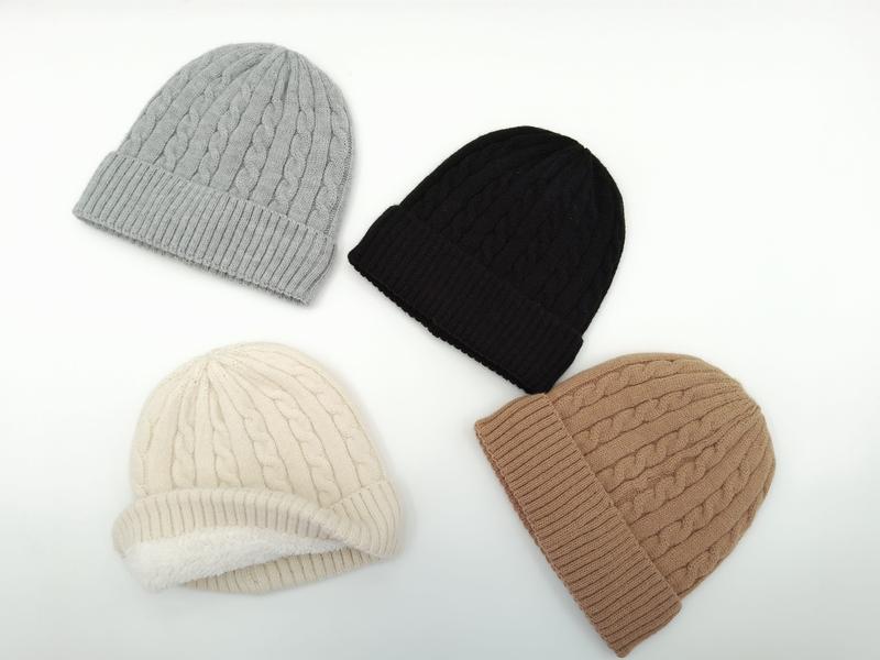 Four cable knit winter beanies in grey, black, cream, and tan laid flat on white background - private label service available