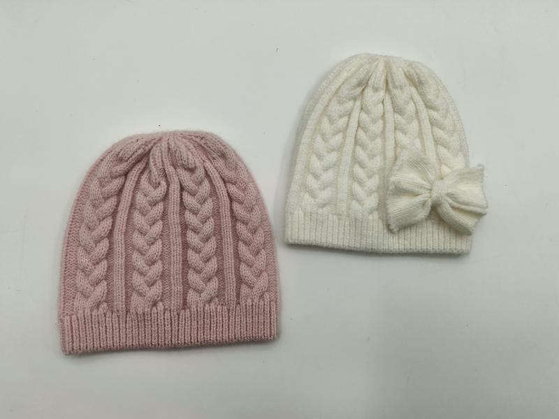 Two cable knit winter beanies side by side, one dusty pink and one cream white with a decorative bow on the side - ODM OEM service available - tiered pricing available ask quote