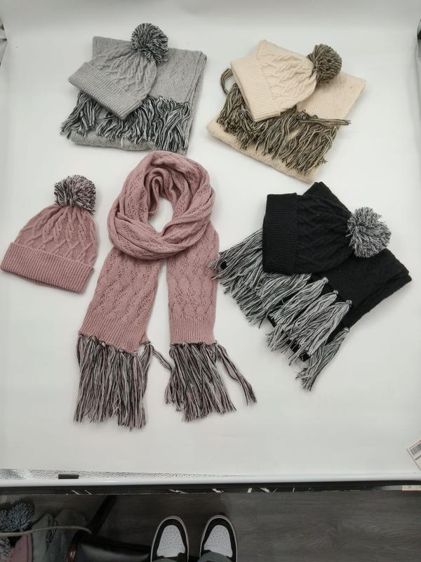 Four cable knit winter hat and scarf sets in gray, cream, pink, and black with pom pom beanies and fringed scarves laid flat - contact for custom design quote