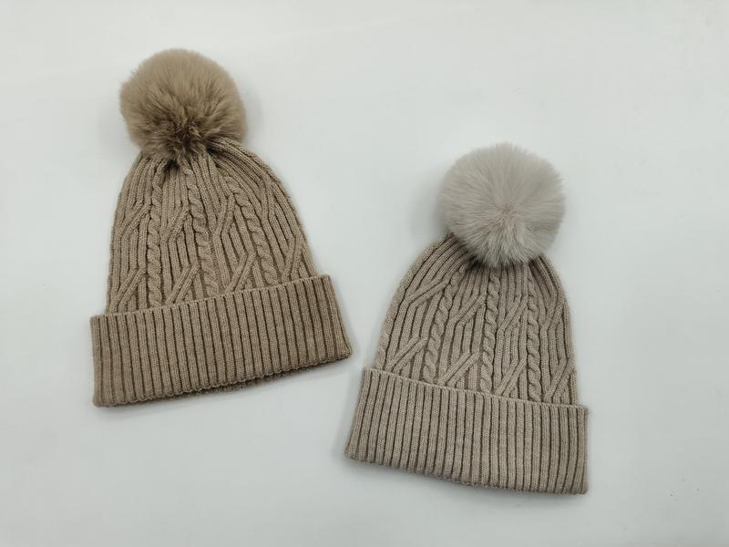 Two cable knit winter beanies with faux fur pom poms in taupe and light grey, displayed on white background - certified scarf manufacturer China - WhatsApp quote in 2 hours