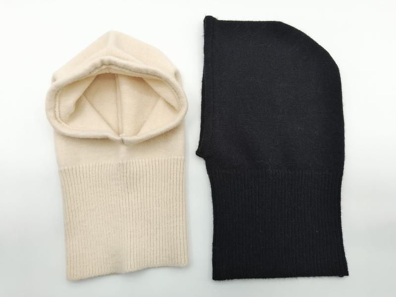 Two knit cashmere balaclavas laid flat on white background, one cream with open face and one solid black, showing ribbed neck detail - BSCI + Oeko-Tex + GRS certified