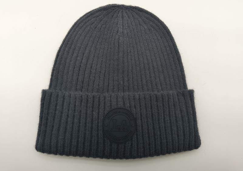 Charcoal grey ribbed knit cuffed beanie hat with circular rubber logo patch reading Change Is Possible, laid flat on white background - Oeko-Tex Standard 100 certified