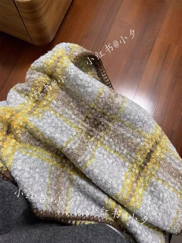 Folded chunky boucle plaid throw blanket in gray, yellow, and beige tones resting on a chair with wood floor background - custom Pantone color matching