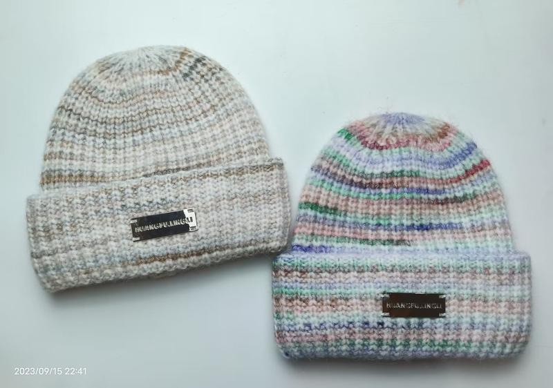 Two chunky knit beanies with folded cuffs: one neutral marled beige, one multicolor pastel striped, both with metal logo labels - boutique retail bulk order