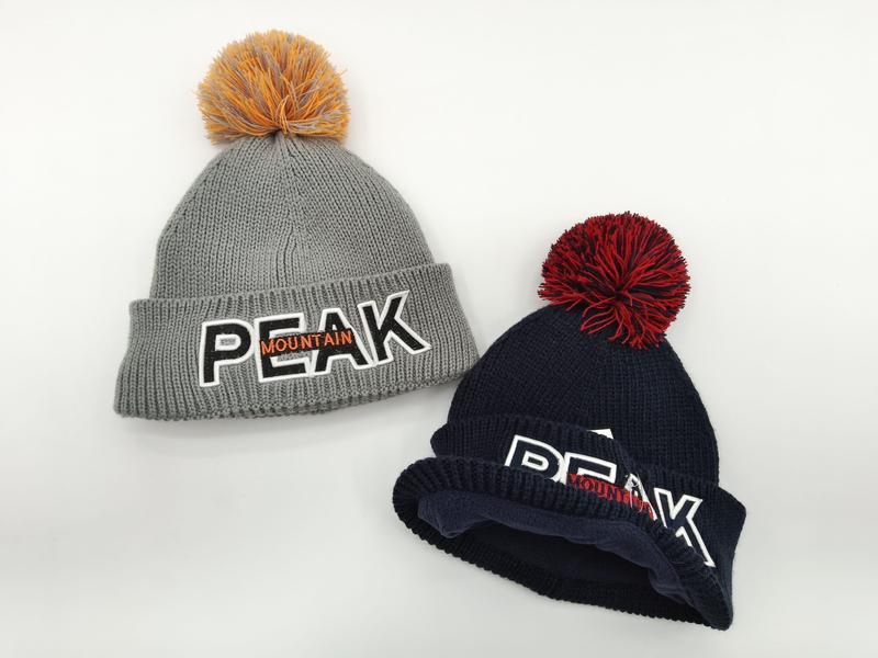 Two chunky knit pom-pom beanies in grey and navy blue with embroidered Peak Mountain logo, displayed on white background - custom size no extra charge
