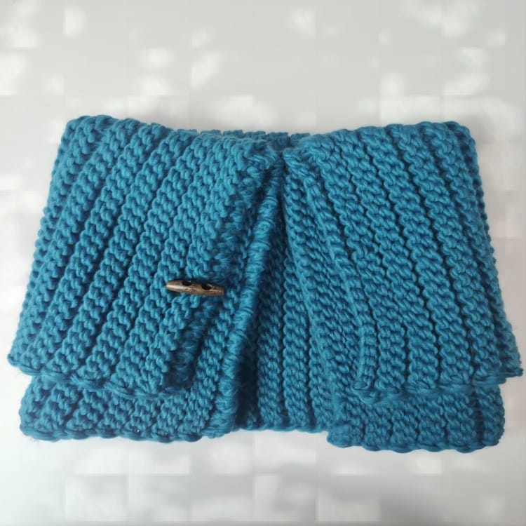 Folded teal chunky knit cowl neck warmer with wooden toggle button closure, ribbed texture, displayed on white surface - wholesale price for USA buyers