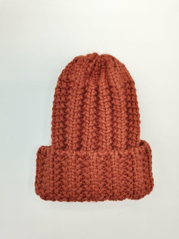 Rust orange chunky ribbed knit beanie hat with folded cuff, laid flat on white background, handmade wool texture - custom packaging design free