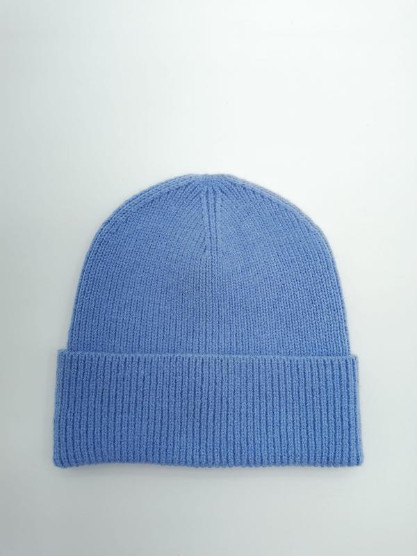 Flat lay of a cornflower blue soft knit beanie hat with folded ribbed cuff on a light grey background - hotel amenity scarf supplier
