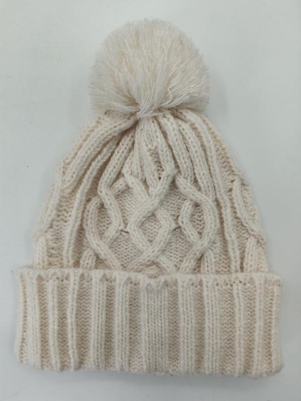 Cream cable knit winter beanie hat with fluffy pom pom on top and ribbed cuff, laid flat on white background - EU REACH compliant material