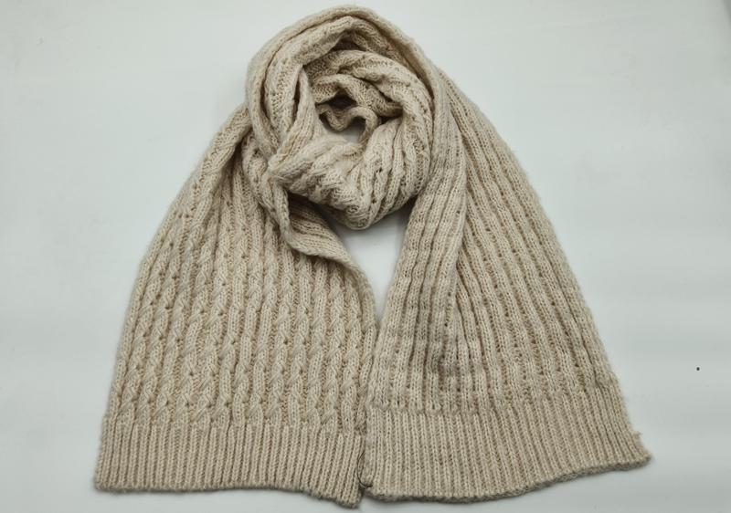 Cream beige cable knit scarf loosely coiled on white background showing textured pattern and ribbed hem ends - corporate gift customization