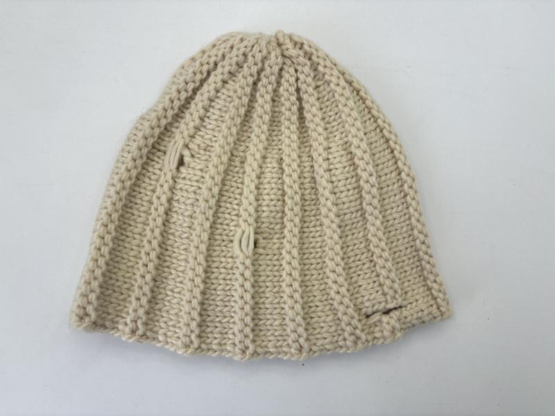 Flat lay of a cream chunky ribbed knit beanie hat in ivory natural yarn, folded to show textured stitch pattern - contact for custom design quote