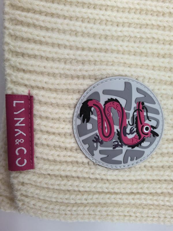 Cream chunky ribbed knit beanie with pink dragon circular rubber patch and pink brand label on textured wool fabric - low MOQ 50pcs trial order