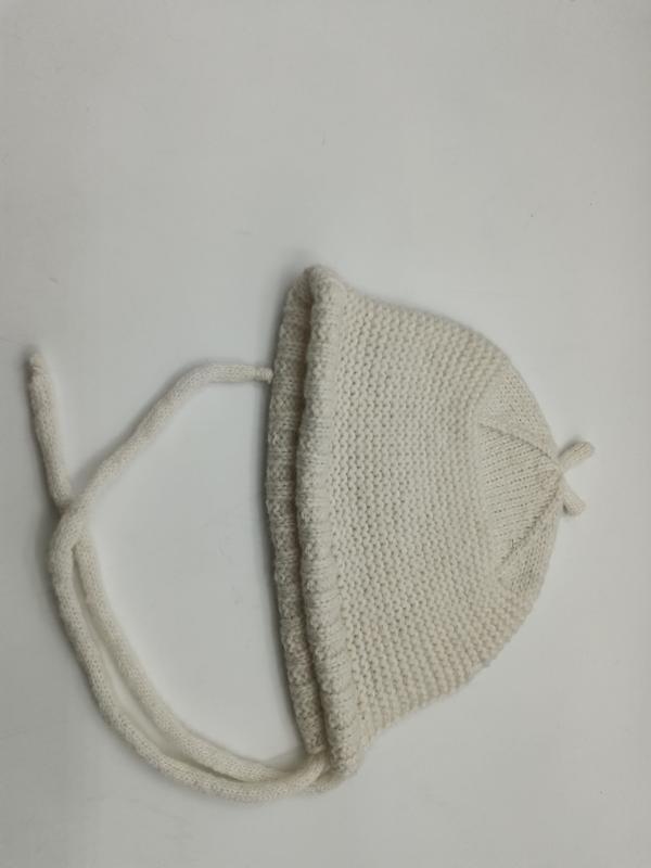Cream ivory hand-knitted baby bonnet with chin tie strings laid flat on white surface, garter stitch texture - hotel amenity scarf supplier