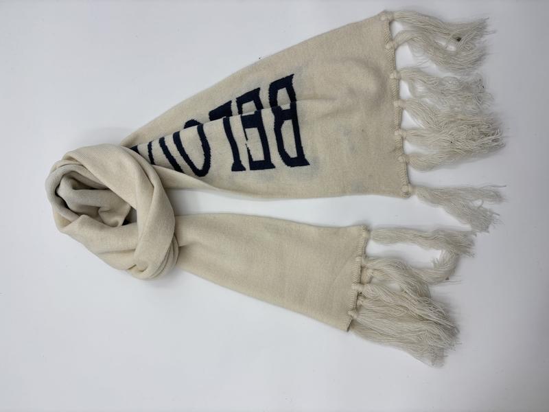 Cream knit scarf with navy blue varsity-style letter print and tassel fringe ends, laid flat on white background - bulk order 20-day delivery