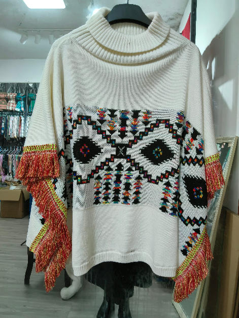 Cream oversized knit turtleneck poncho with multicolor Aztec geometric pattern and red fringe-trimmed sleeves on mannequin - WhatsApp quote in 2 hours