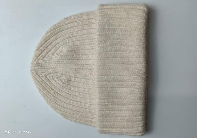 Cream ribbed knit beanie hat laid flat on white surface, showing folded cuff and classic rib stitch texture in natural off-white color - hotel amenity scarf supplier