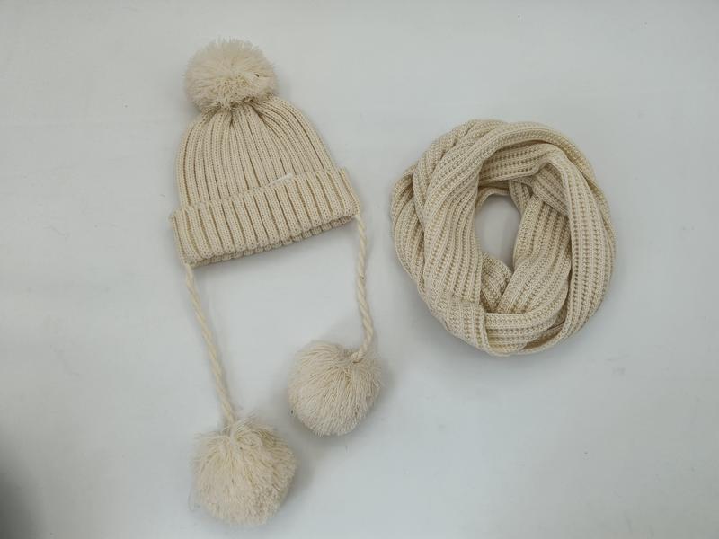 Cream ribbed knit winter beanie hat with pom-poms and braided ties alongside a matching infinity loop scarf set - certified scarf manufacturer China - request quote reply same day