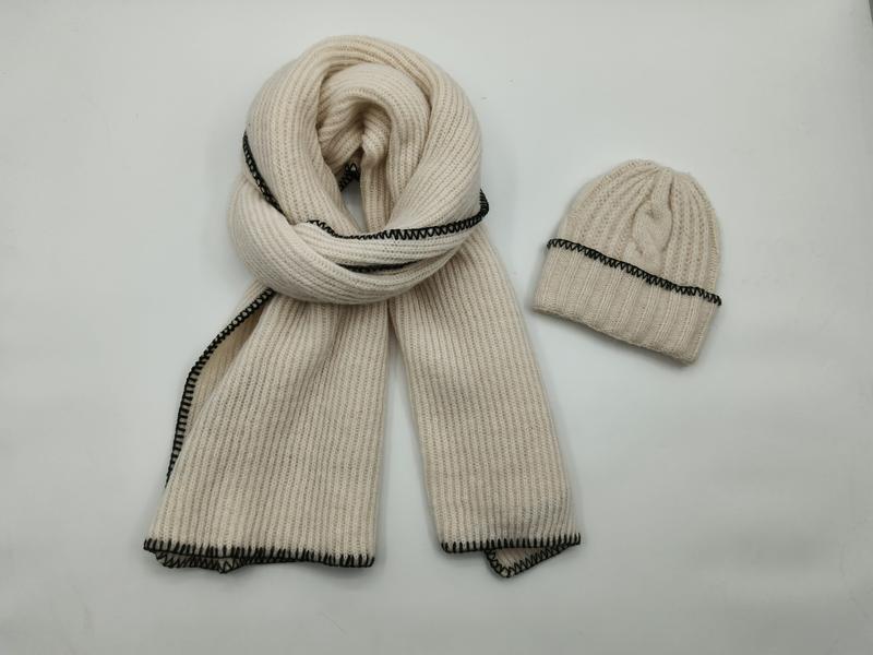 Cream ribbed knit scarf coiled next to matching beanie hat, both featuring black blanket stitch edge detailing on white background - sample order 10pcs available