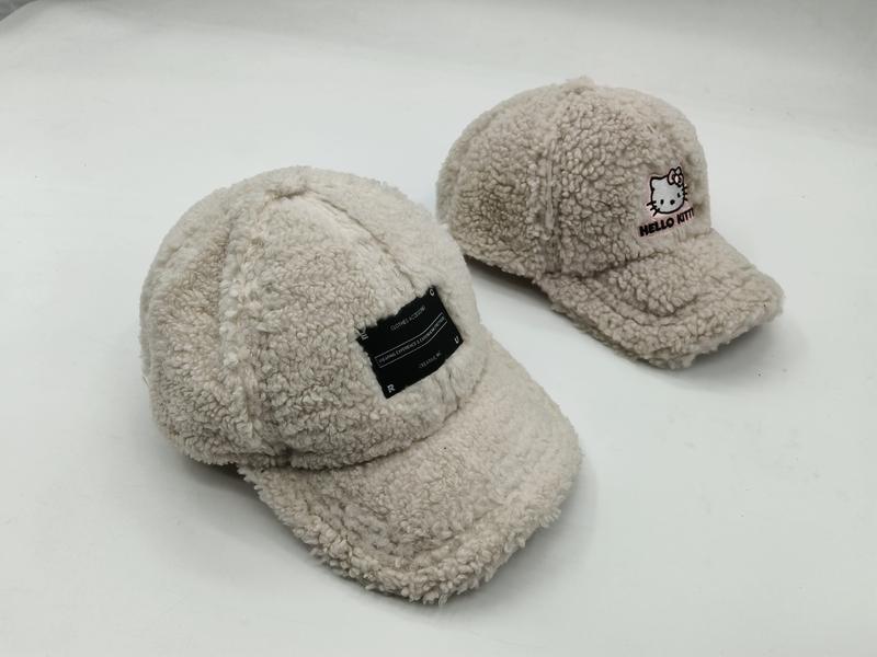 Two cream sherpa fleece baseball caps side by side, one with a black label patch and one with Hello Kitty embroidery on white background - custom Pantone color matching