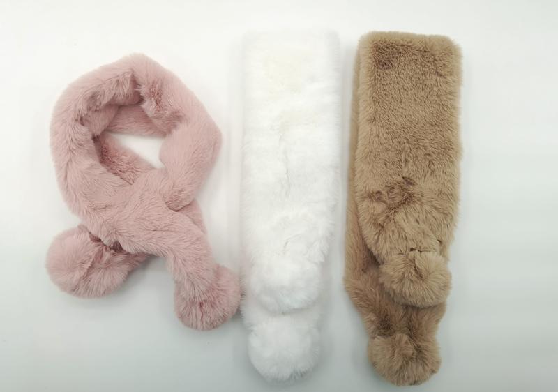 Three fluffy faux fur pull-through scarves with pom pom ends in blush pink, white, and tan laid flat on white background - wholesale price for Europe buyers
